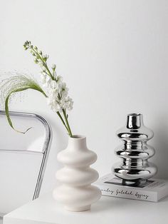 a white vase sitting on top of a table next to a book and flower pot