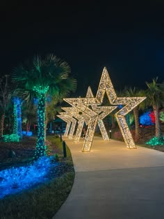 a large lighted star in the middle of a walkway surrounded by palm trees and blue lights