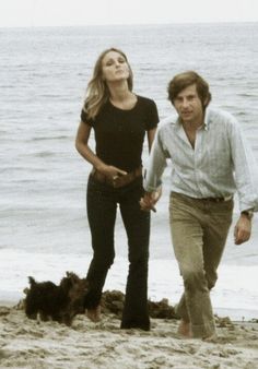 a man and woman walking on the beach with a dog next to them in front of the ocean