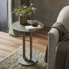 a living room with a chair, table and vase on the floor in front of a window