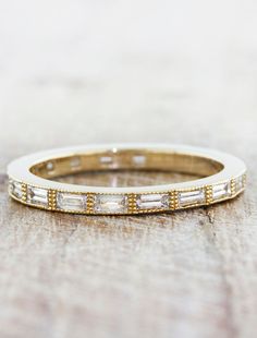 a wedding band with baguettes and diamonds on the side, sitting on a wooden surface