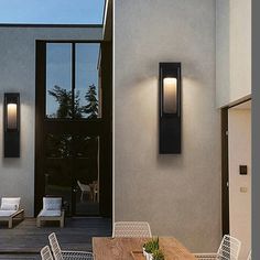 an outdoor dining area with table, chairs and lights on the side of the house