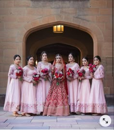 a group of women standing next to each other in front of a building with red flowers