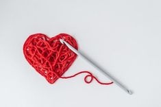 a red crochet heart with a needle in the middle on a white background