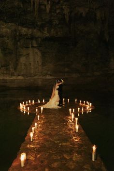 a bride and groom standing on a dock surrounded by candles