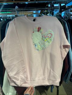 a person is holding up a pink sweatshirt with a heart on it in front of some clothes