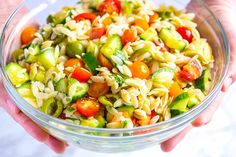 a person holding a glass bowl filled with pasta salad