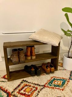 a wooden shoe rack with shoes on it next to a rug and potted plant