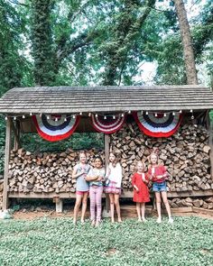 three girls standing in front of a firewood stand with american flag decorations on it