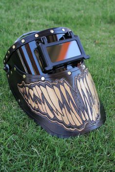 a helmet sitting on top of a lush green field next to a cell phone in it's mouth