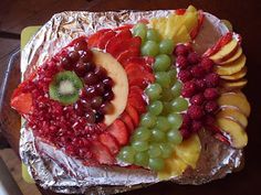 a fruit platter on aluminum foil with grapes, apples, kiwi and raspberries