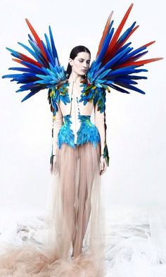 a woman with large blue and red feathers on her head standing in front of a white backdrop