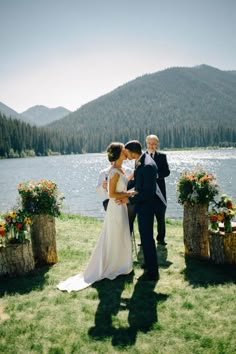 a bride and groom standing next to each other in front of a lake with flowers