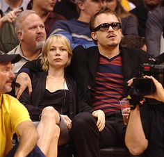 two people sitting next to each other in front of a crowd at a basketball game