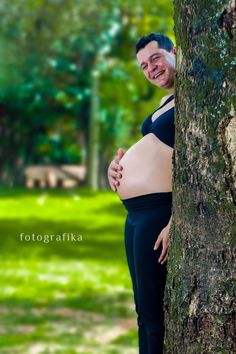 a pregnant woman standing next to a tree