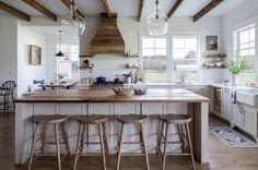 a kitchen with white walls and wooden beams on the ceiling, along with four stools