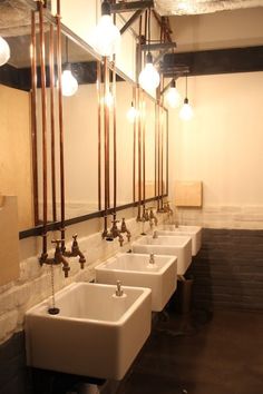 a row of sinks in a public restroom with lights on the wall and mirrors above them