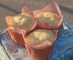 three muffins wrapped in pink paper sitting on top of a blue and white cloth