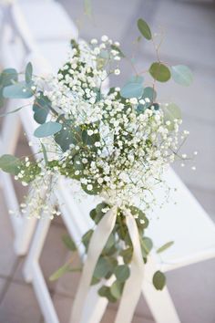 a bouquet of baby's breath sitting on top of a white chair with greenery