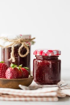 two jars filled with jam sitting on top of a wooden bowl next to strawberries