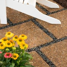 a white rocking chair sitting on top of a stone floor next to flowers and grass