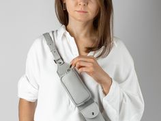 a woman wearing a white shirt holding onto a gray camera strap with her hand on the shoulder