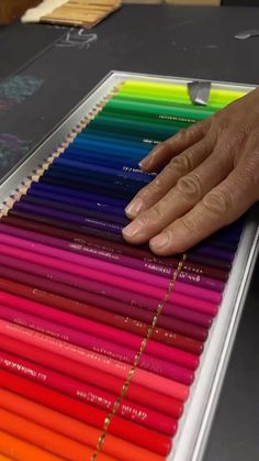 a person's hand is on the top of a box of colored pencils