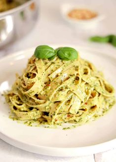 a white plate topped with pasta covered in sauce and garnished with green leaves