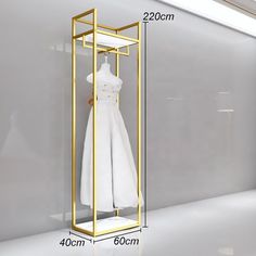 a white dress hanging on a gold frame in front of a gray wall with measurements