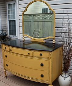 an old dresser with a mirror on top is sitting in front of a house next to a potted plant