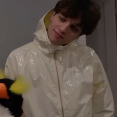 a boy in a white raincoat holding a stuffed penguin