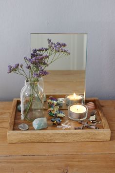 a vase with flowers and rocks on a wooden tray in front of a glass mirror