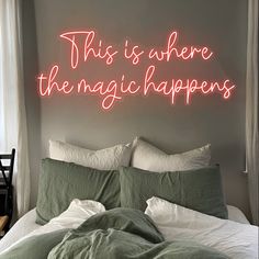 this is where the magic happens neon sign above a bed with white sheets and pillows