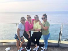 three women posing for the camera on top of a building with water in the background