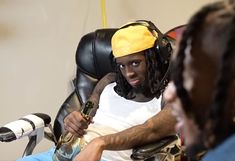 a man with dreadlocks sitting in a chair holding a cell phone to his ear