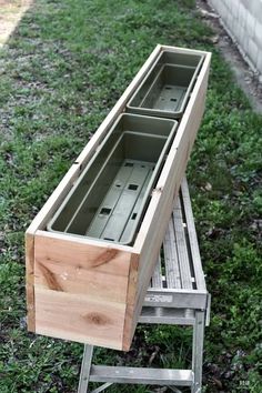 two wooden drawers sitting on top of a metal step ladder in the grass next to a brick wall