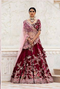 a woman in a red and pink lehenga standing next to a white wall