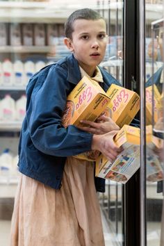 a young boy is holding boxes in front of a glass display case at a grocery store