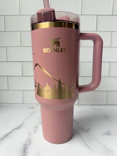 a pink and gold travel mug with a straw sticking out of the lid on a marble countertop