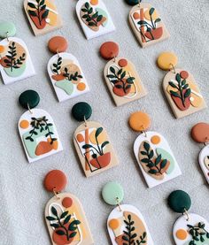 many different shapes and sizes of earrings on a white tablecloth with grey linen behind them