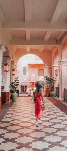 a woman in a red dress and hat walking down a hall with tiled flooring