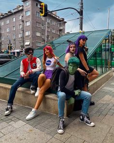 four people are sitting on a ledge in front of a traffic light and some buildings