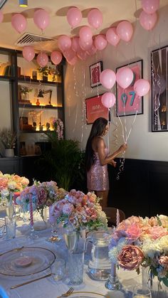 a woman standing in front of a table filled with pink and white flowers next to balloons