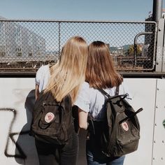 two girls with backpacks standing in front of a wall