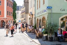 many people are walking down the street in front of some shops and restaurants on cobblestone streets