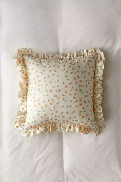 a pillow with ruffles on it sitting on top of a white bed sheet