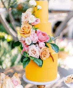 a yellow wedding cake with pink and orange flowers on the top, surrounded by other desserts