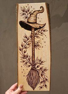 a hand holding up a wooden plaque with an image of a hat on top of it