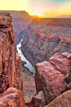 the sun is setting at the edge of a cliff overlooking a river and canyon below