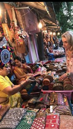 two women looking at fabrics on display in an open air market with people standing around